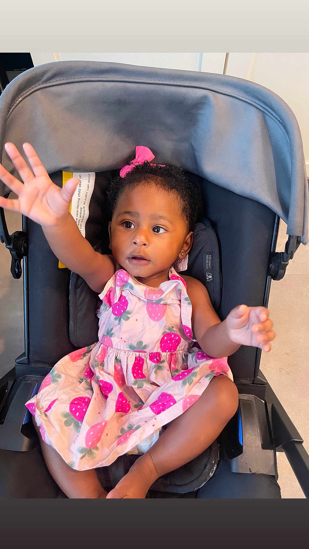 Xena joined the competition — help win amazing prizes! child, toddler, baby, stroller, dress, pink_bow, curly_hair, reaching_hand, indoor, seat, cute, person, infant, fashion, expression, portrait, young_child, clothing, sitting, attention