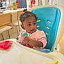 Xena joined the competition — help win amazing prizes! toddler, child, high_chair, toy, kitchen, curly_hair, pink_clothing, plastic_toy, table, chair, indoor, baby, person, face, earrings, curious, colorful, cabinet, plant, household