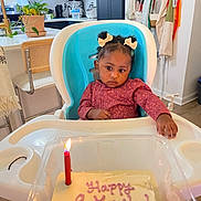 Xena joined the competition — help win amazing prizes! baby, high_chair, cake, candle, kitchen, curly_hair, hair_bows, birthday, celebration, child, food, table, person, indoor, furniture, pink_icing, light, curious, clothing, seat