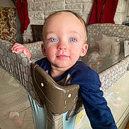 Nicholas is registered to the contest to win money with this photo: toddler, child, playpen, blue_eyes, rosy_cheeks, fireplace, stockings, holiday_decor, indoors, curious, face, hand, clothing, baby, home, furniture, smile, person, portrait, cozy