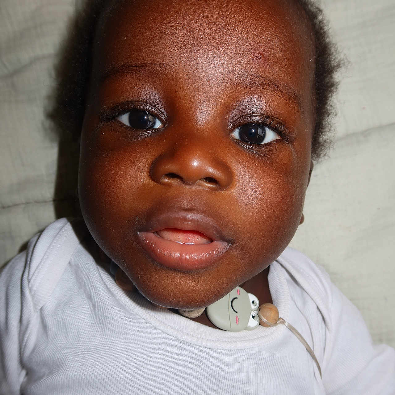 Swann-Isaac a rejoint le concours — aidez-le/la à gagner de superbes lots ! baby, bedding, child, close_up, clothing, curious_expression, eyelashes, eyes, face, hair, indoors, infant, lips, mouth_open, necklace, nose, pacifier_clip, person, portrait, white_shirt