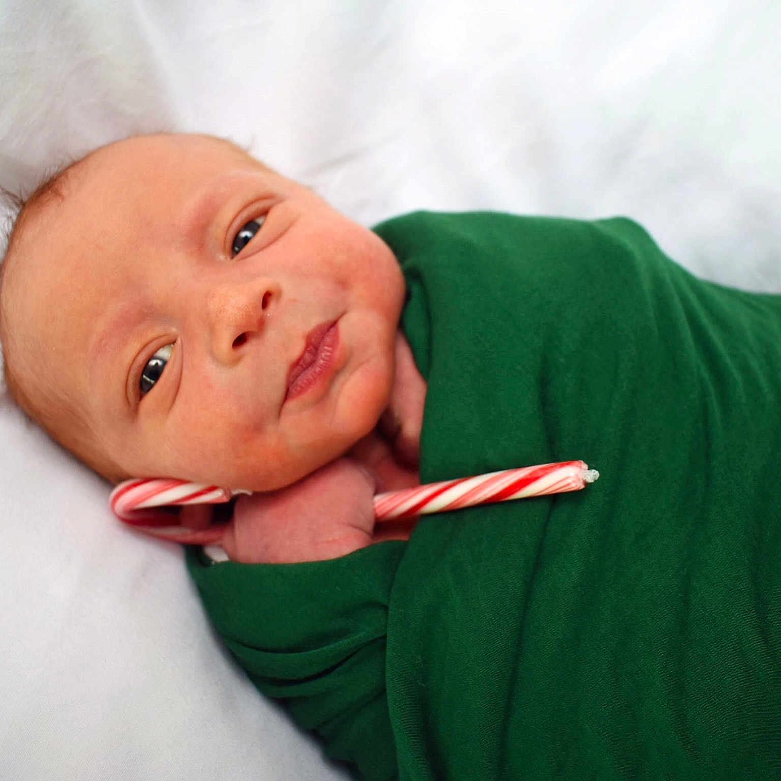Gideon is registered to the contest to win money with this photo: baby, candy_cane, child, closeup, cozy, cute, face, green_blanket, hand, holiday, indoors, infant, lying_down, newborn, peaceful, portrait, resting, skin, soft_background, swaddled