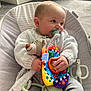 baby, pacifier, knitted_sweater, plush_toy, colorful_toy, baby_chair, carpet, pet_bed, indoor, child, cute, infant, cozy, smiling, hand, face, person, comfort, soft_toys, casual
