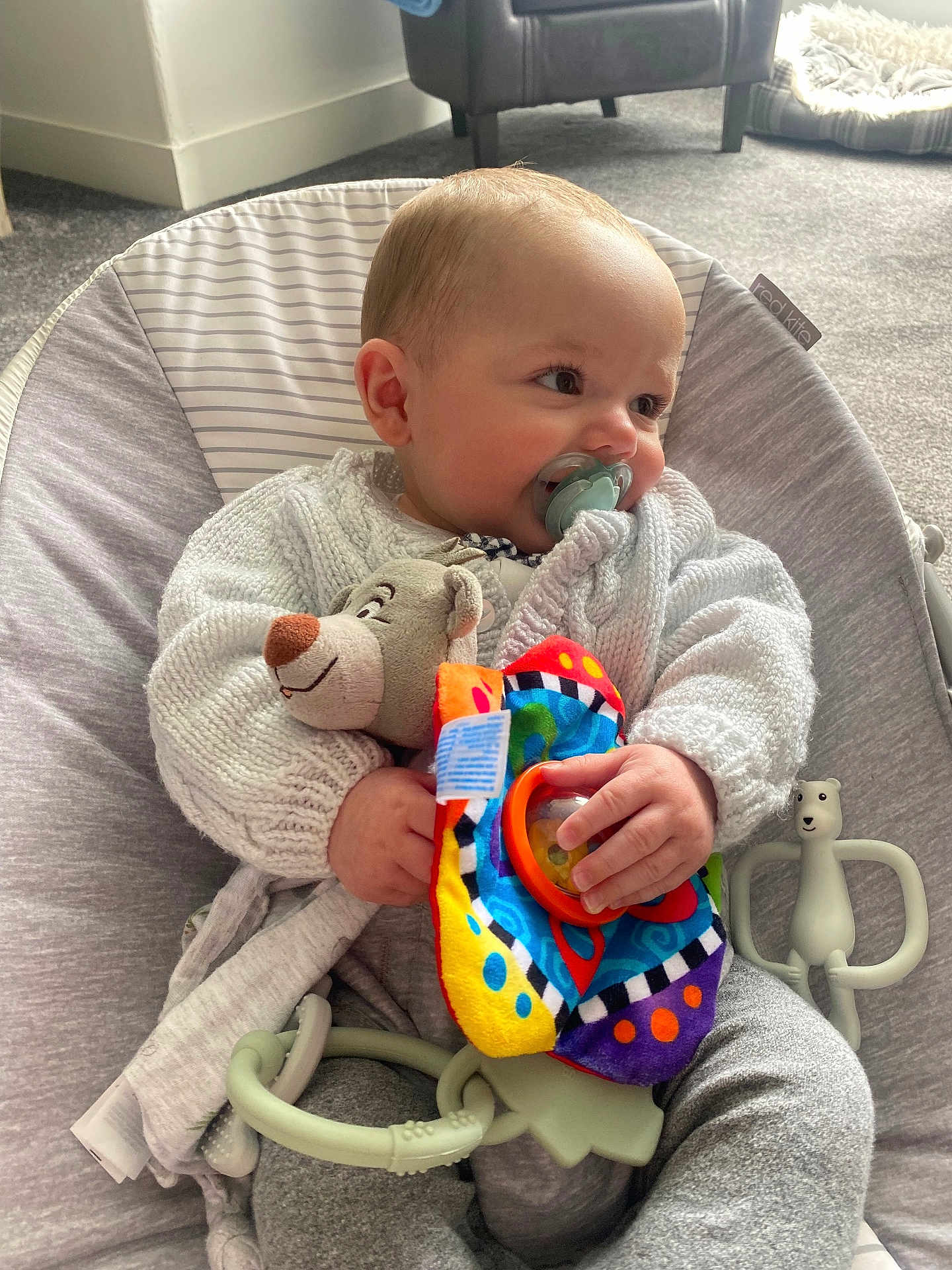 Justin is registered to the contest to win money with this photo: baby, pacifier, knitted_sweater, plush_toy, colorful_toy, baby_chair, carpet, pet_bed, indoor, child, cute, infant, cozy, smiling, hand, face, person, comfort, soft_toys, casual