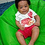 baby, child, indoor, bean_bag, green, curly_hair, smiling, white_shirt, red_shorts, teddy_bear, roses, furniture, carpet, sitting, happy, cute, person, portrait, relaxed, home