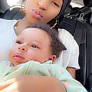 Nyari is registered to the contest to win money with this photo: woman, baby, child, car_interior, headwrap, earrings, onesie, strawberry_pattern, natural_light, holding, portrait, face, skin, hand, seatbelt, seat, window, black_hair, expression, closeup