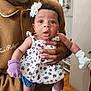 Nyari is registered to the contest to win money with this photo: baby, infant, adult, hand, flower_headband, mittens, dress, shoes, indoor, flooring, wood, person, clothing, face, expression, curious, holding, home, decor, portrait