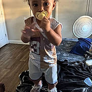 Azrael Young joined the competition — help win amazing prizes! toddler, child, baby, pacifier, standing, indoors, bedroom, bed, fan, sneakers, clothing, portrait, curly_hair, smiling, home, furniture, blanket, wood_floor, photography, playful