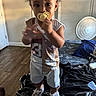 toddler, child, baby, pacifier, standing, indoors, bedroom, bed, fan, sneakers, clothing, portrait, curly_hair, smiling, home, furniture, blanket, wood_floor, photography, playful
