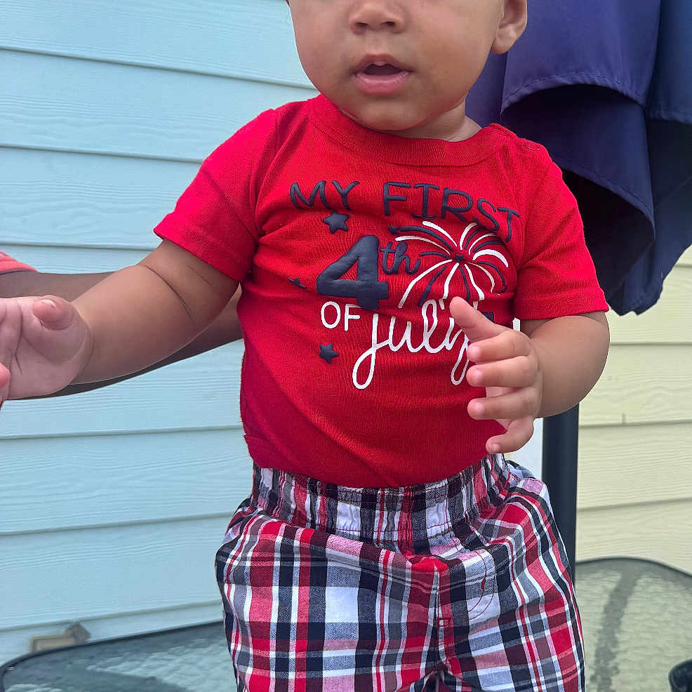 Azrael Young joined the competition — help win amazing prizes! child, toddler, baby, standing, portrait, red_hat, red_shirt, plaid_shorts, red_shoes, patriotic_clothing, fourth_of_july, outdoor, patio, glass_table, house, siding, lantern, curtain, fashion, smiling