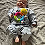 baby, infant, smile, toy, plush_toy, colorful, blanket, clothing, comfortable, happy, cute, lying_down, soft_texture, indoors, child, feet, hand, face, casual, cozy