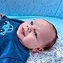 baby, infant, blue_sweater, car_design, blanket, floral_pattern, star_pattern, lying_down, portrait, cute, soft_texture, indoors, child, face, head, skin, expression, eyes, ear, cozy