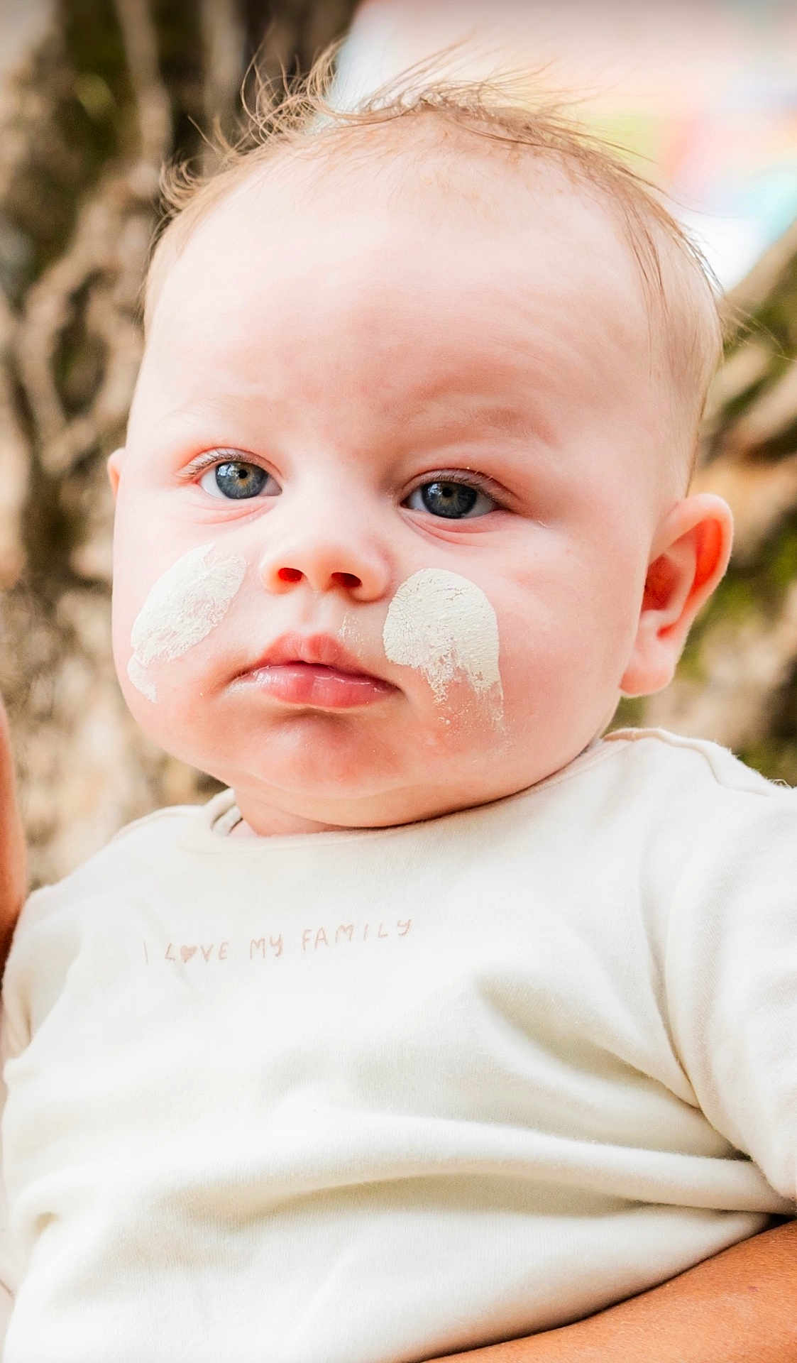 Jarrah is registered to the contest to win money with this photo: baby, blue_eyes, cheeks, child, close_up, cream, cute, expressionless, face, human, infant, natural_light, outdoor, person, portrait, skin, soft_focus, text_on_clothing, white_shirt, young_child