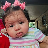 Mackenzie is registered to the contest to win money with this photo: baby, child, portrait, face, hair_bow, pink_bow, striped_dress, drooling, chubby_cheeks, indoor, person, holding, cute, infant, expression, closeup, toddler, hand, skin, casual_clothing