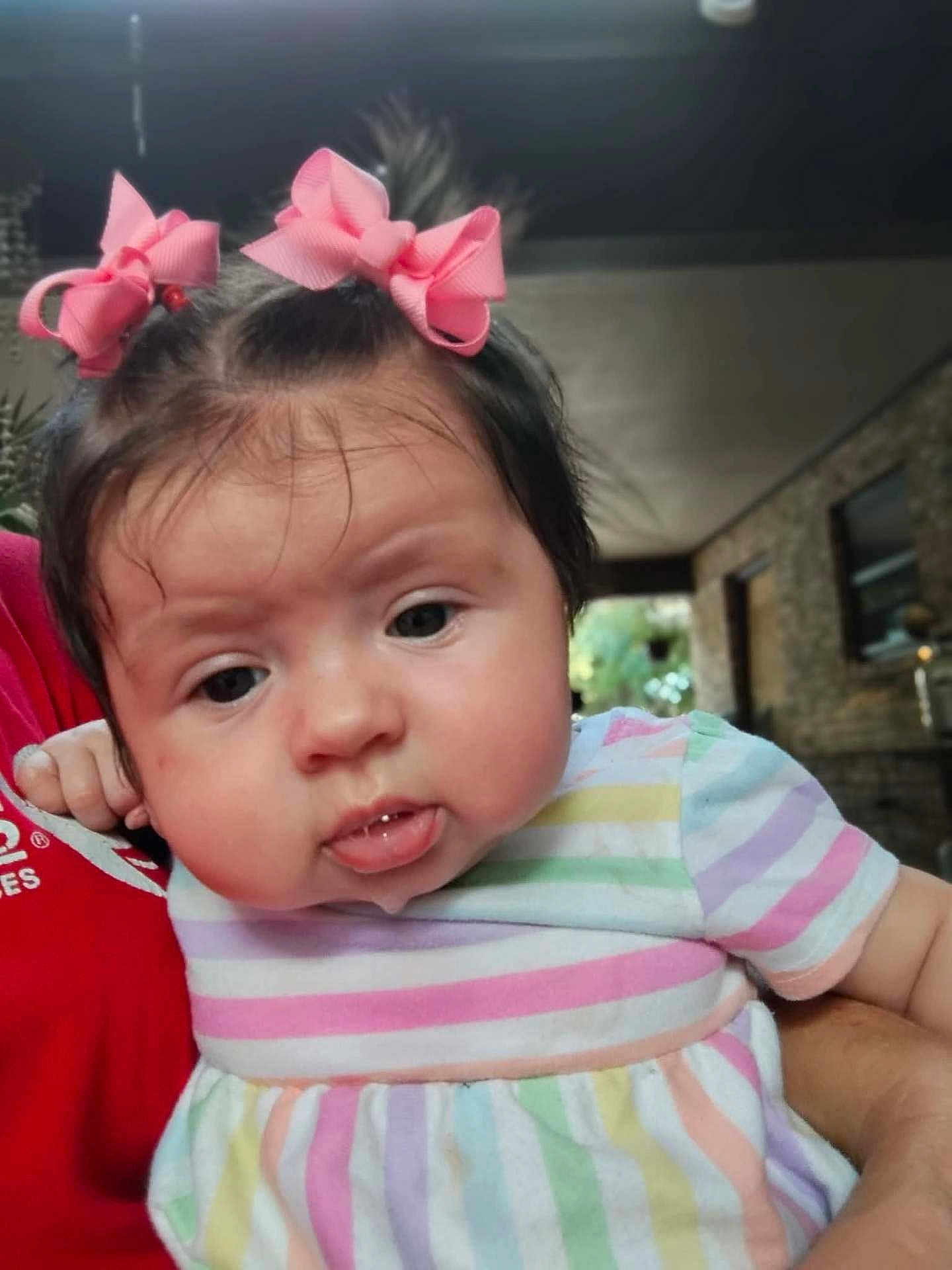 Mackenzie is registered to the contest to win money with this photo: baby, child, portrait, face, hair_bow, pink_bow, striped_dress, drooling, chubby_cheeks, indoor, person, holding, cute, infant, expression, closeup, toddler, hand, skin, casual_clothing