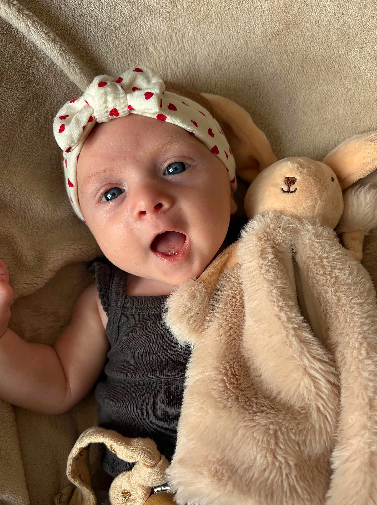 Emy a rejoint le concours — aidez-le/la à gagner de superbes lots ! baby, headband, heart_pattern, plush_toy, bunny, blanket, soft_texture, infant, cute, surprised_expression, child, face, blue_eyes, sleepwear, indoors, cozy, closeup, skin, hand, lying_down