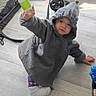 toddler, child, hooded_jacket, bottle, sitting, floor, indoor, toy, stroller, casual, cozy, clothing, person, baby, cute, hand, footwear, playful, expression, young_child