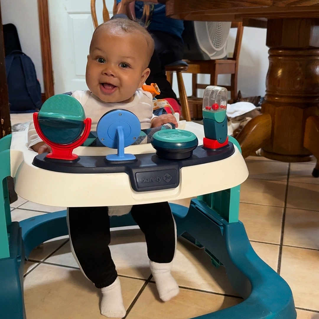 Donte joined the competition — help win amazing prizes! baby, casual, chair, child, clothing, family, furniture, glasses, happy, home, indoor, person, phone, seated, smiling, table, tile_floor, toys, walker, woman