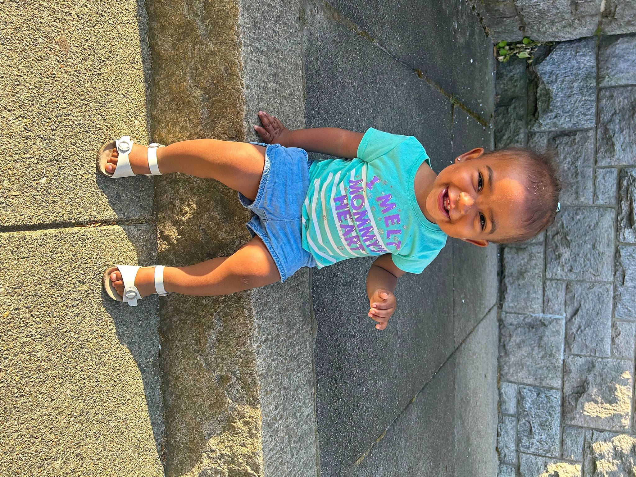 Amya is registered to the contest to win money with this photo: asphalt, child, concrete, denim, electric_blue, fun, happy, human_leg, joy, leisure, person, road, road_surface, shorts, sidewalk, smile, street, t_shirt, thigh, toddler