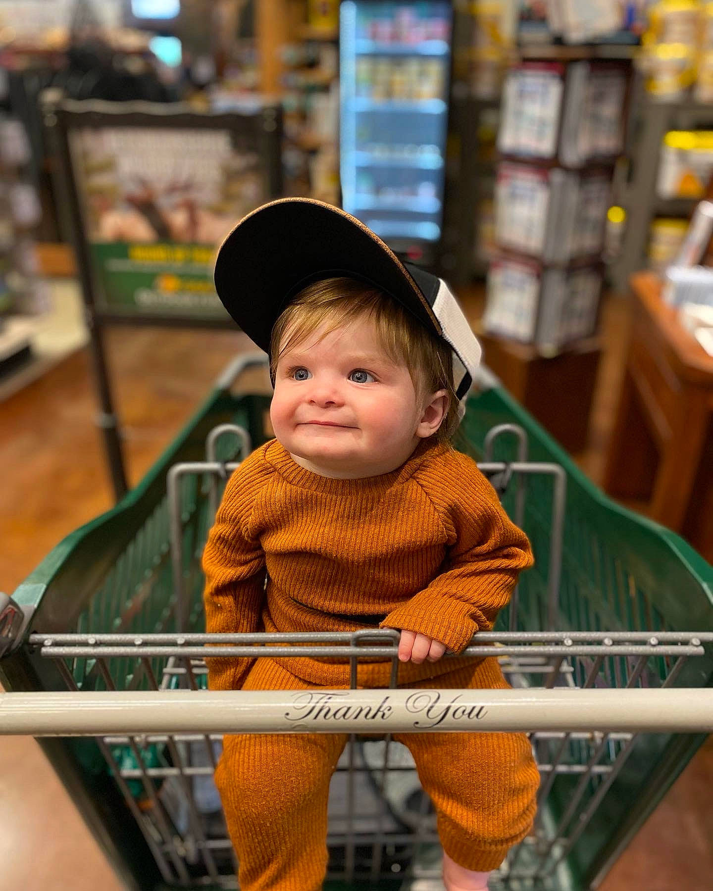 Cory is registered to the contest to win money with this photo: baby, baby_toddler_clothing, bookcase, cap, child, comfort, customer, fun, joy, leisure, person, photograph, publication, retail, shelf, shopping_cart, sitting, smile, snapshot, standing