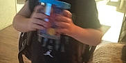 Ryden joined the competition — help win amazing prizes! child, indoor, drinking, cup, straw, backpack, diaper, shirt, couch, carpet, floor, kitchen, furniture, person, blurry, young_child, home, casual, standing, curly_hair