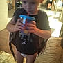 child, indoor, drinking, cup, straw, backpack, diaper, shirt, couch, carpet, floor, kitchen, furniture, person, blurry, young_child, home, casual, standing, curly_hair