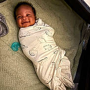 Chosen joined the competition — help win amazing prizes! baby, blanket, child, comfort, cozy, crib, cute, dinosaur_pattern, face, happy, indoors, infant, newborn, pacifier, person, resting, sleeping_area, smile, soft_surface, swaddled