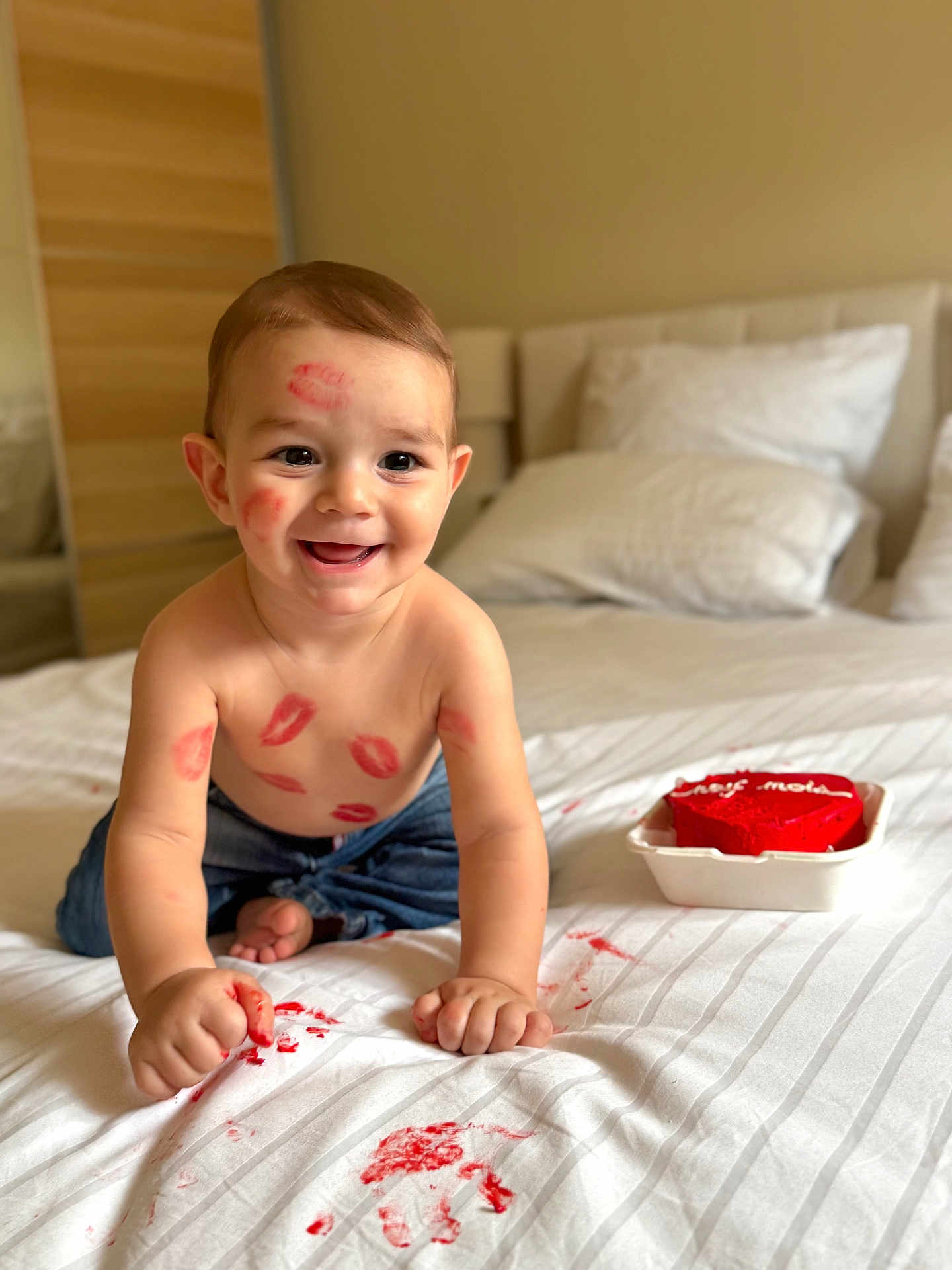 Sidrin participe au concours pour gagner de l'argent avec cette photo : baby, child, smiling, lipstick_marks, red_cake, bed, white_sheets, handprints, red_smudges, shirtless, jeans, happy, indoor, crawling, face, messy, cute, celebration, love, playful