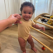 Ocean joined the competition — help win amazing prizes! baby, child, smiling, curly_hair, onesie, wooden_floor, hand_holding, play_structure, toy, indoors, curtains, cheerful, standing, person, floor, light, room, support, cute, happy