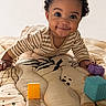 Ocean is registered to the contest to win money with this photo: baby, child, curly_hair, striped_clothing, toy_blocks, smile, lying_down, mattress, patterned_bedding, indoor, playtime, cute, happy, infant, person, portrait, bright_eyes, hand, soft_lighting, warm_colors