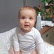 Victor participe au concours pour gagner de l'argent avec cette photo : baby, child, infant, sitting, hand_holding, cushion, white_clothing, indoor, plant, bottle, face, curious, cute, person, home, furniture, table, skin, head, eyes