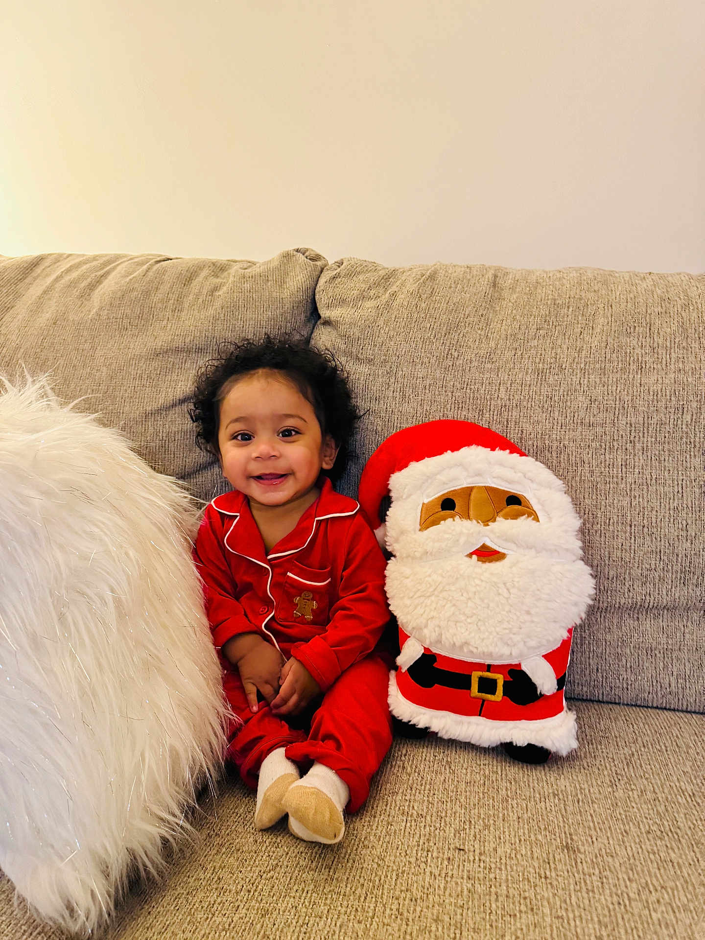 Reginald joined the competition — help win amazing prizes! toddler, child, smiling, red_pajamas, plush_toy, santa_claus, couch, white_pillow, indoor, holiday_theme, curly_hair, happy, cozy, home, soft_texture, cute, festive, seated, portrait, young_child