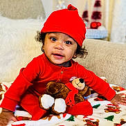 Reginald joined the competition — help win amazing prizes! toddler, child, red_clothing, red_hat, plush_toy, teddy_bear, blanket, christmas_theme, holiday_decor, sofa, indoor, cute, smiling, festive, cozy, portrait, bright_colors, happy, curly_hair, warm_lighting