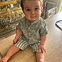 Tyam participe au concours pour gagner de l'argent avec cette photo : baby, child, table, indoor, curious, clothing, striped_shorts, patterned_shirt, face, eyes, hand, foot, model_airplanes, furniture, wood, casual, sitting, cute, person, young