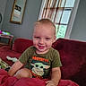 Greyson joined the competition — help win amazing prizes! child, toddler, smiling, portrait, indoor, couch, blanket, red_blanket, shirt, grogu, star_wars, sitting, home, window, curtains, wall, mirror, furniture, happy, closeup