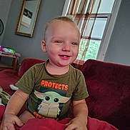 Greyson joined the competition — help win amazing prizes! toddler, child, baby, smiling, happy, portrait, sitting, sofa, blanket, red_blanket, t_shirt, grogu, star_wars, living_room, window, curtains, indoor, home, short_hair, face