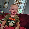 toddler, child, baby, smiling, happy, portrait, sitting, sofa, blanket, red_blanket, t_shirt, grogu, star_wars, living_room, window, curtains, indoor, home, short_hair, face