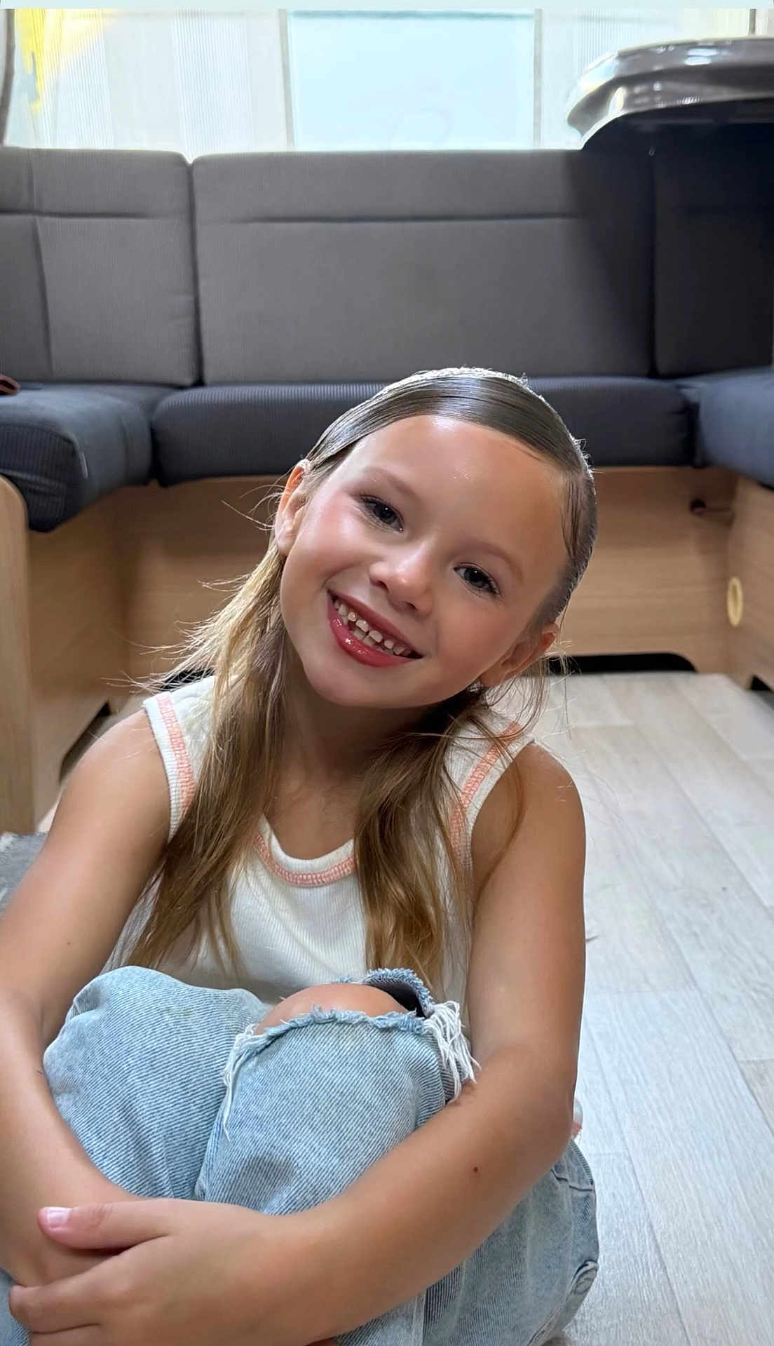 Brianna participe au concours pour gagner de l'argent avec cette photo : child, girl, smiling, long_hair, jeans, ripped_jeans, tank_top, sitting, floor, wooden_floor, indoor, living_room, couch, furniture, casual_clothing, happy, portrait, young, cute, relaxed