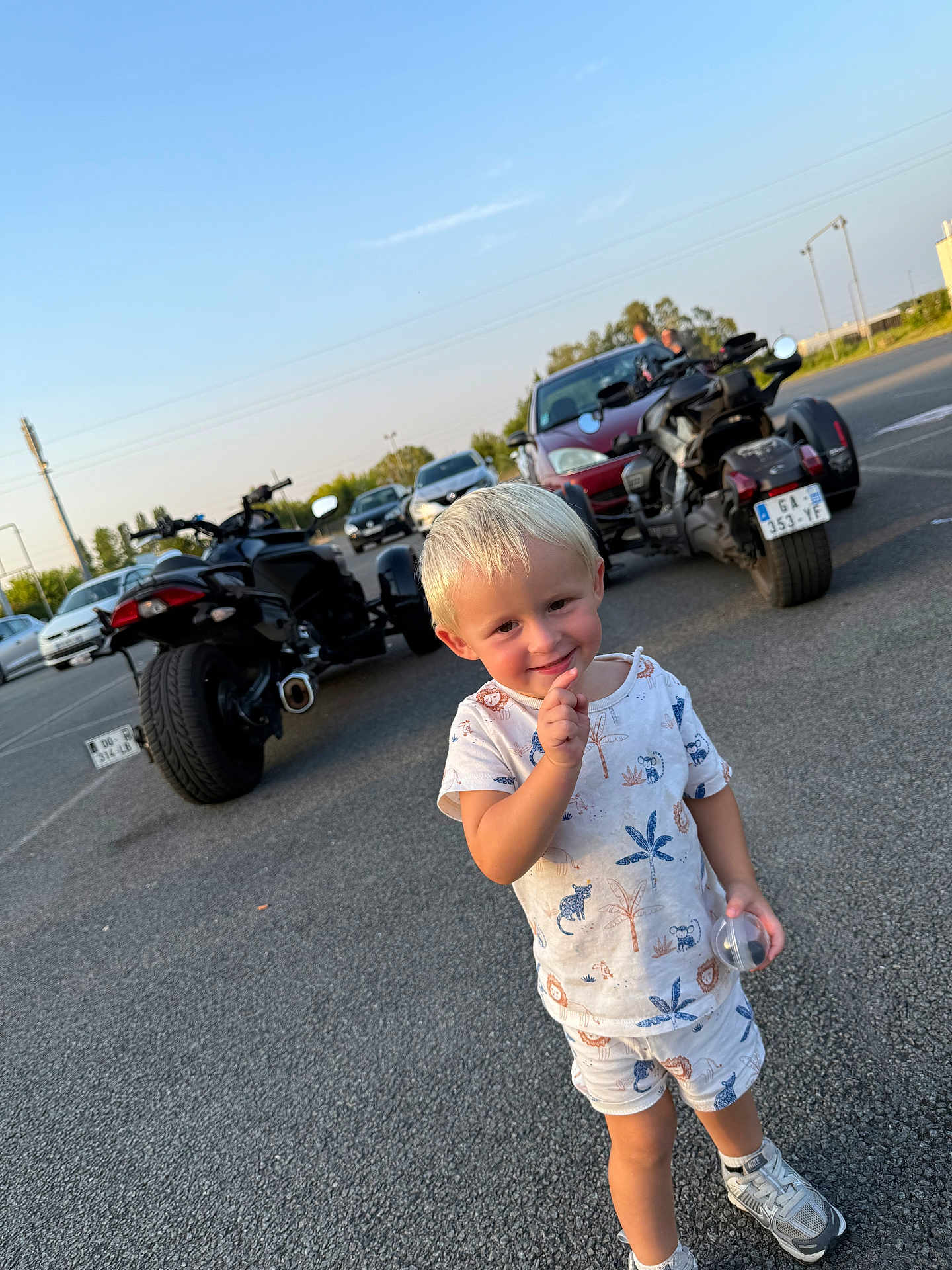 Lemon a rejoint le concours — aidez-le/la à gagner de superbes lots ! child, toddler, blond_hair, smiling, parking_lot, motorcycle, car, pajamas, shorts, sneakers, outdoor, daytime, asphalt, blue_sky, vehicle, cute, person, holding_object, casual_clothing, playful