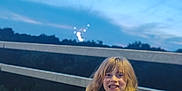 Gracey joined the competition — help win amazing prizes! blonde_hair, bridge, cartoon, casual_clothing, child, evening, fun, lighting, nature, outdoor, person, playful, railing, sky, smile, trees, tshirt, twilight, water, young