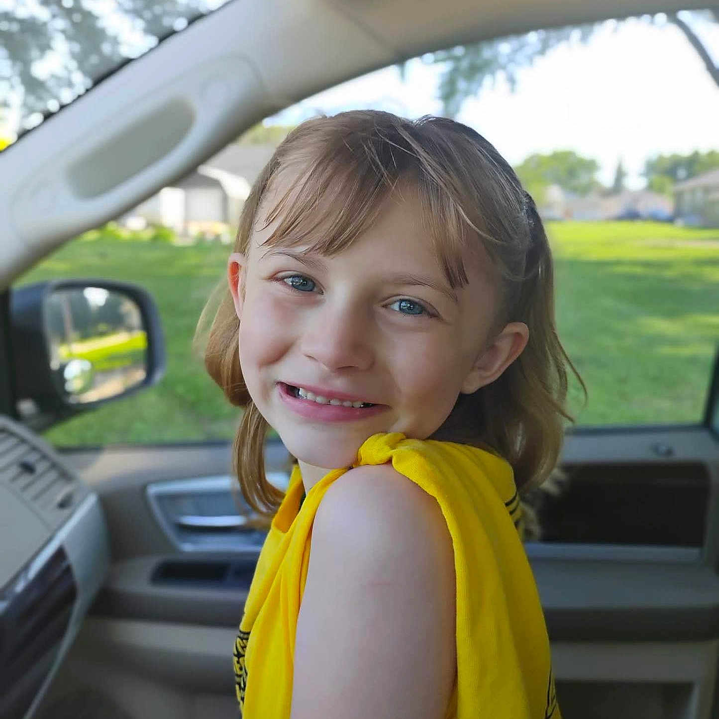 Gracey is registered to the contest to win money with this photo: blue_eyes, car_interior, casual_clothing, child, daylight, face, girl, greenery, hair, happy, human, natural_light, portrait, seat, side_view, smiling, vehicle, window, yellow_shirt, young