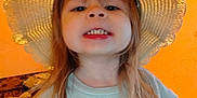 Rosey joined the competition — help win amazing prizes! bed, blanket, casual_clothing, child, cute, happy, hat, home, indoor, kid, long_hair, orange_wall, person, playful, portrait, smile, sunhat, sweatshirt, teeth, young_child