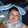baby, child, smiling, dinosaur_shirt, blanket, patterned_blanket, cute, portrait, indoor, happy, infant, clothing, face, person, toddler, soft_texture, cozy, reaching_out, light_shadow, closeup
