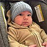 Nikko Lee is registered to the contest to win money with this photo: baby, infant, child, hoodie, hat, knit_hat, car_seat, warning_label, beige_clothing, gray_fabric, cozy, cute, portrait, indoor, person, closeup, young_child, chubby_cheeks, casual_wear, seated