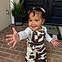 black_door, brick_porch, child, cow_print, curly_hair, earrings, festive, greenery, happy, holiday, necklace, outdoor, overalls, pigtails, plant, portrait, reaching_hand, smiling, toddler, white_shirt
