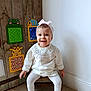 baby, child, girl, white_clothing, headband, smile, sitting, wooden_chair, floor_tile, wall, wooden_panel, decorative_toys, animal_shapes, indoor, cute, happy, footwear, toddler, head, person