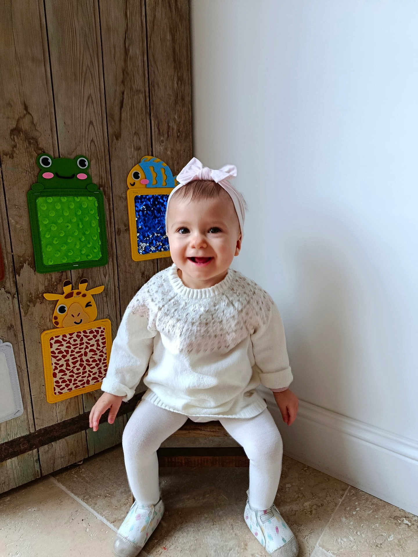 Lina participe au concours pour gagner de l'argent avec cette photo : baby, child, girl, white_clothing, headband, smile, sitting, wooden_chair, floor_tile, wall, wooden_panel, decorative_toys, animal_shapes, indoor, cute, happy, footwear, toddler, head, person