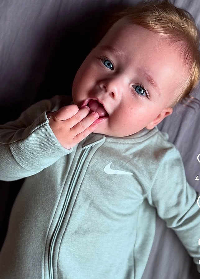 Joris a rejoint le concours — aidez-le/la à gagner de superbes lots ! baby, child, face, blue_eyes, blonde_hair, hand, clothing, nike_logo, zip_up, portrait, cute, infant, playful, expression, lying_down, indoor, skin, young_child, person, closeup