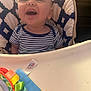 Ryder joined the competition — help win amazing prizes! baby, high_chair, striped_shirt, smile, toy, indoor, child, happy, face, seat, cushion, blue, white, pattern, infant, playful, mouth_open, clothing, person, young
