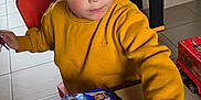 Ethan a rejoint le concours — aidez-le/la à gagner de superbes lots ! child, yellow_sweater, toy_car, table, bottle, indoor, play, young_child, red_chair, workbench, toy_tools, floor_tiles, window, furniture, person, short_hair, concentration, plastic_toys, casual_clothing, home
